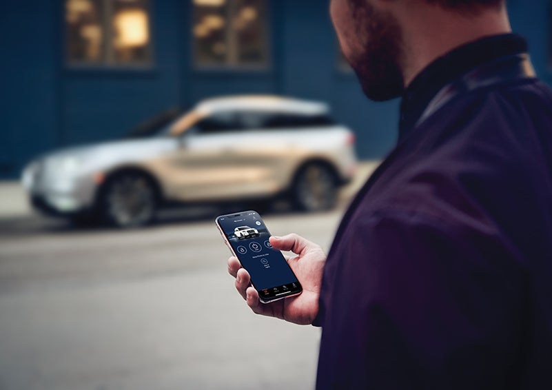 A person is shown interacting with a smartphone to connect to a Lincoln vehicle across the street. | Holmes Tuttle Lincoln in Tucson AZ